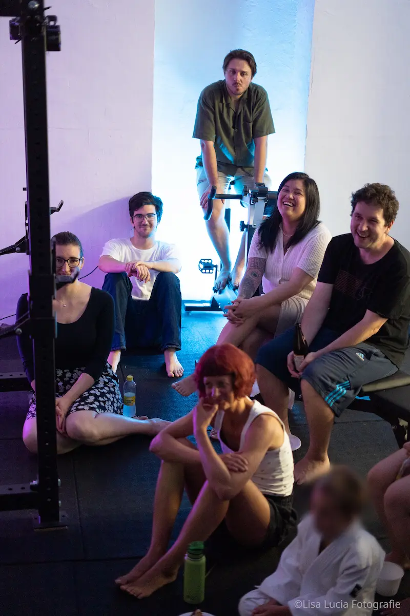 Teamabend bei Hocus Chokus BJJ Wien – die Gruppe sitzt entspannt beisammen und schaut einer Zaubershow zu, stimmungsvolles Discolicht
