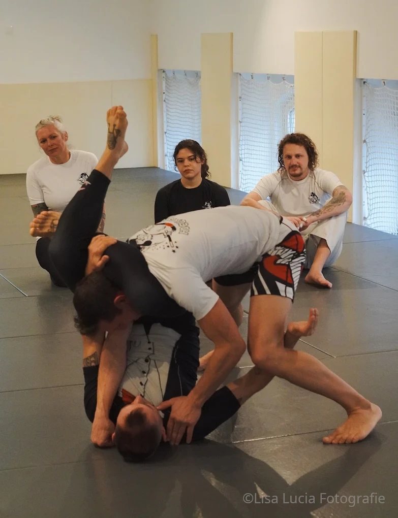 No-Gi Brazilian Jiu-Jitsu bei Hocus Chokus in Wien – Submission-Versuch aus der Guard, die Trainingsgruppe schaut zu